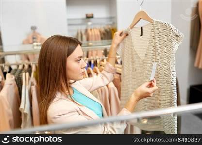 shopping, fashion, sale and people concept - young woman choosing clothes in mall or clothing store and looking at top price tags. woman choosing clothes at clothing store. woman choosing clothes at clothing store