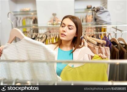shopping, fashion, sale and people concept - young woman choosing clothes in mall or clothing store. woman choosing clothes at clothing store