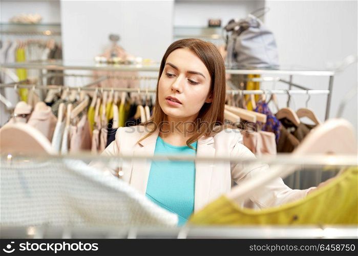 shopping, fashion, sale and people concept - young woman choosing clothes in mall or clothing store. woman choosing clothes at clothing store