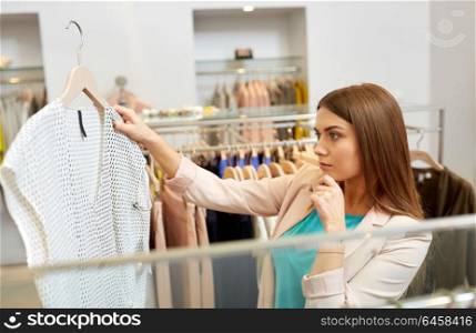 shopping, fashion, sale and people concept - young woman choosing shirt in mall or clothing store. woman choosing clothes at clothing store