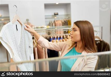 shopping, fashion, sale and people concept - young woman choosing shirt in mall or clothing store. woman choosing clothes at clothing store. woman choosing clothes at clothing store
