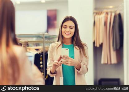 shopping, fashion, style, technology and people concept - happy woman with smartphone taking mirror selfie at clothing store. woman taking mirror selfie by smartphone at store