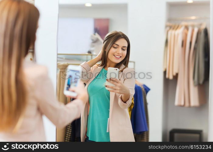 shopping, fashion, style, technology and people concept - happy woman with smartphone taking mirror selfie at clothing store