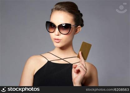 shopping, finances, fashion, people and luxury concept - beautiful young woman in elegant black sunglasses with credit card over gray background