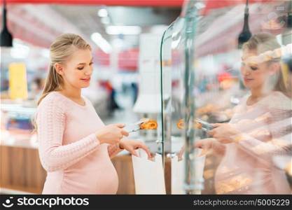 shopping, food, pregnancy and people concept - happy pregnant woman with paper bag and tongs buying buns at grocery store or supermarket. pregnant woman with bag buying buns at grocery