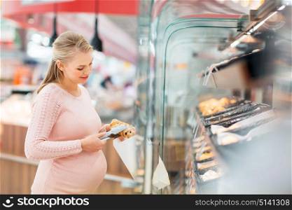 shopping, food, pregnancy and people concept - happy pregnant woman with paper bag and tongs buying buns at grocery store or supermarket. pregnant woman with bag buying buns at grocery