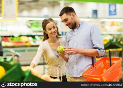 shopping, food, sale, consumerism and people concept - happy couple buying apples at grocery store or supermarket. happy couple buying apples at grocery store