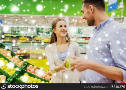 shopping, food, sale, consumerism and people concept - happy couple buying apples at grocery store or supermarket over snow. happy couple buying apples at grocery store