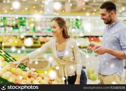 shopping, food, sale, consumerism and people concept - happy couple buying apples at grocery store or supermarket over snow. happy couple buying apples at grocery store