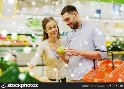 shopping, food, sale, consumerism and people concept - happy couple buying apples at grocery store or supermarket over snow . happy couple buying apples at grocery store