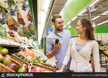 shopping, food, sale, consumerism and people concept - happy couple buying avocado at grocery store or supermarket