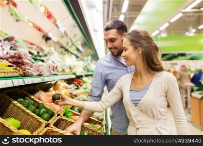 shopping, food, sale, consumerism and people concept - happy couple buying avocado at grocery store or supermarket. happy couple buying avocado at grocery store