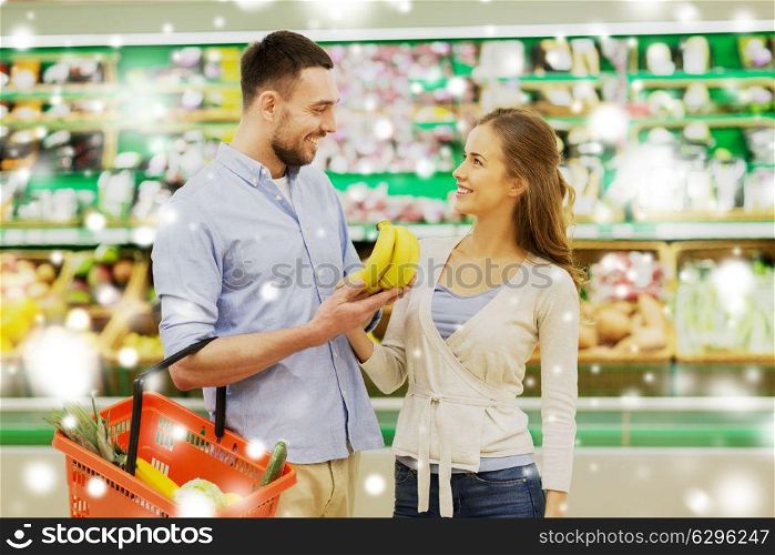 shopping, food, sale, consumerism and people concept - happy couple buying bananas at grocery store or supermarket over snow. happy couple buying bananas at grocery store