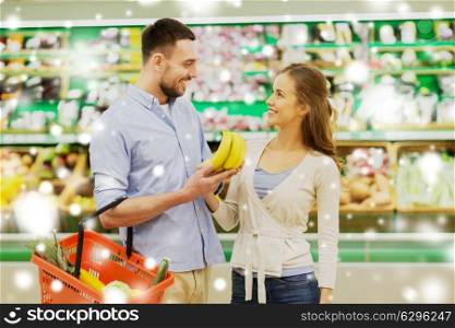 shopping, food, sale, consumerism and people concept - happy couple buying bananas at grocery store or supermarket over snow. happy couple buying bananas at grocery store