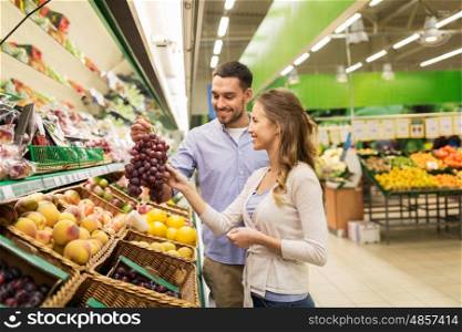 shopping, food, sale, consumerism and people concept - happy couple buying grapes at grocery store or supermarket