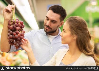 shopping, food, sale, consumerism and people concept - happy couple buying grapes at grocery store or supermarket