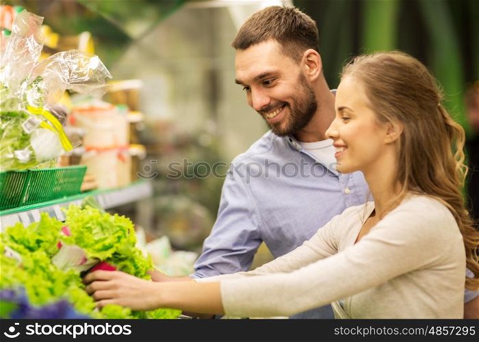 shopping, food, sale, consumerism and people concept - happy couple buying lettuce at grocery store or supermarket