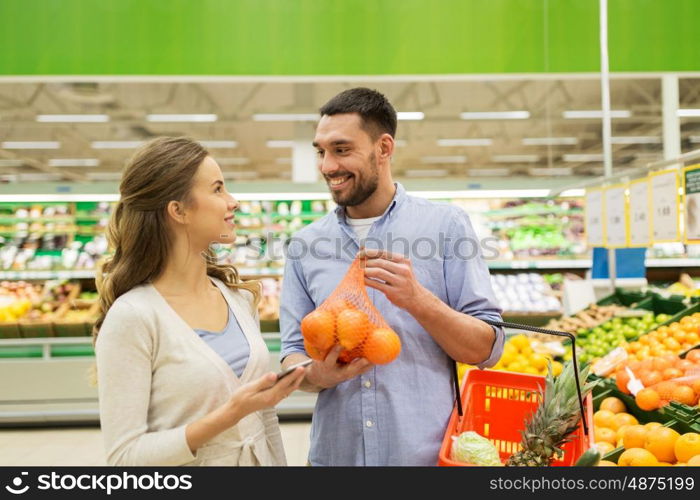 shopping, food, sale, consumerism and people concept - happy couple buying oranges at grocery store or supermarket