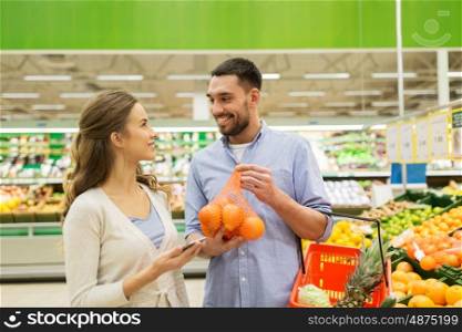 shopping, food, sale, consumerism and people concept - happy couple buying oranges at grocery store or supermarket