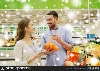 shopping, food, sale, consumerism and people concept - happy couple buying oranges at grocery store or supermarket over snow. happy couple buying oranges at grocery store