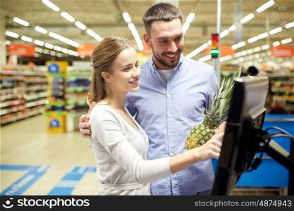 shopping, food, sale, consumerism and people concept - happy couple buying pineapple at grocery store or supermarket self-service cash register