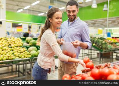 shopping, food, sale, consumerism and people concept - happy couple buying tomatoes at grocery store or supermarket