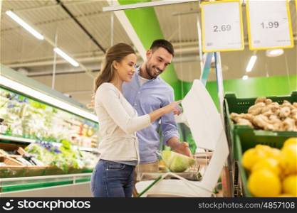 shopping, food, sale, consumerism and people concept - happy couple weighing cabbage on scale at grocery store or supermarket