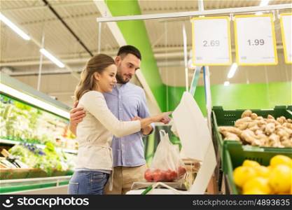 shopping, food, sale, consumerism and people concept - happy couple weighing tomatoes on scale at grocery store or supermarket