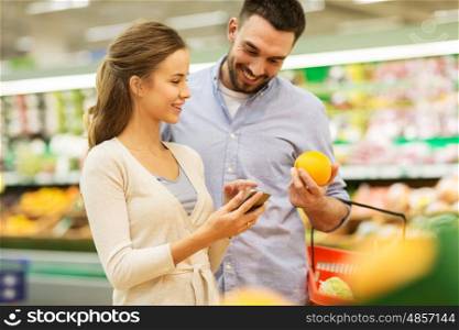 shopping, food, sale, consumerism and people concept - happy couple with smartphone buying oranges at grocery store or supermarket