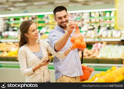 shopping, food, sale, consumerism and people concept - happy couple with smartphone buying oranges at grocery store or supermarket