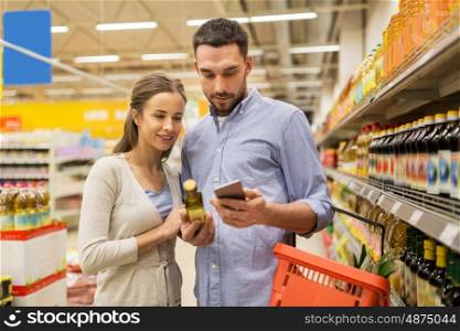shopping, food, sale, consumerism and people concept - happy couple with smartphone buying olive oil at grocery store or supermarket