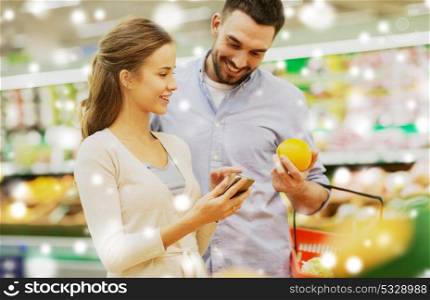 shopping, food, sale, consumerism and people concept - happy couple with smartphone buying oranges at grocery store or supermarket over snow. couple with smartphone buying oranges at grocery