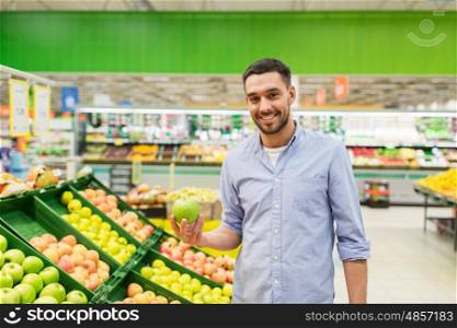 shopping, food, sale, consumerism and people concept - happy man buying green apples at grocery store or supermarket
