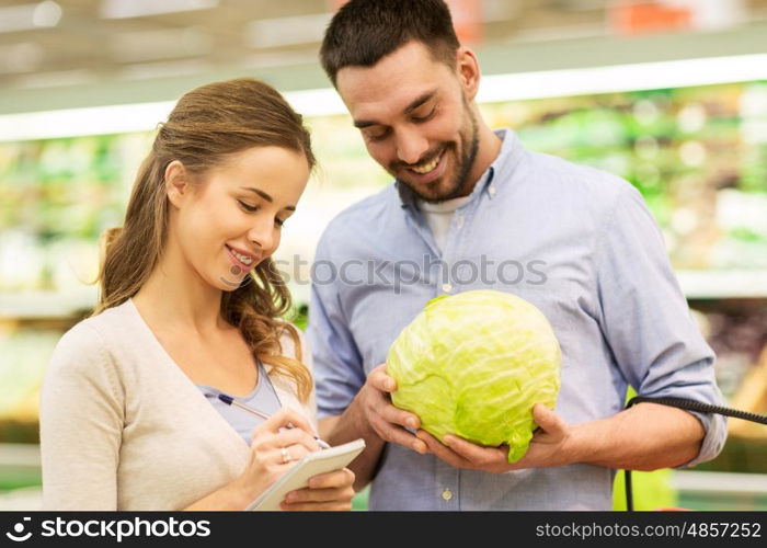 shopping, food, sale, consumerism and people concept - happy young couple with basket and notebook buying cabbage at grocery store or supermarket