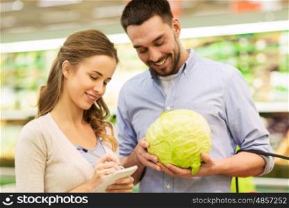 shopping, food, sale, consumerism and people concept - happy young couple with basket and notebook buying cabbage at grocery store or supermarket