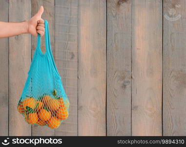 Shopping for groceries without plastic bags. Zero waste concept. A man"s hand holds an eco-friendly reusable bag with organic fruits. Copy space, wood background