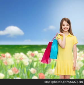 shopping, happiness and people concept - smiling little girl in yellow dress with shopping bags