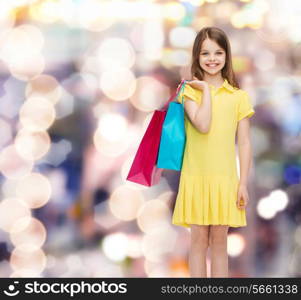 shopping, happiness and people concept - smiling little girl in yellow dress with shopping bags