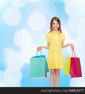 shopping, happiness and people concept - smiling little girl in yellow dress with shopping bags