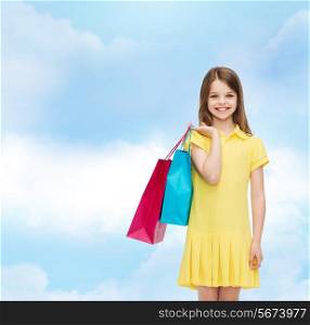 shopping, happiness and people concept - smiling little girl in yellow dress with shopping bags