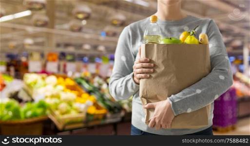 shopping, healthy eating and eco friendly concept - close up of woman with paper bag full of food over supermarket on background. close up of woman with paper bag full of food