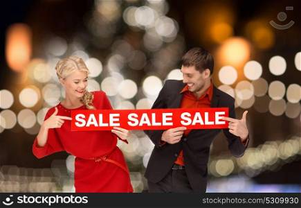 shopping, holidays and people concept - couple with red sale sign over christmas lights background. couple with red sale sign over christmas lights