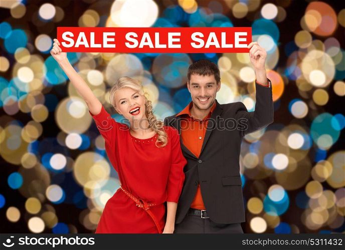 shopping, holidays and people concept - couple with red sale sign over christmas lights background. couple with red sale sign over christmas lights
