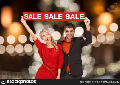 shopping, holidays and people concept - couple with red sale sign over christmas tree lights background. couple with red sale sign over christmas lights