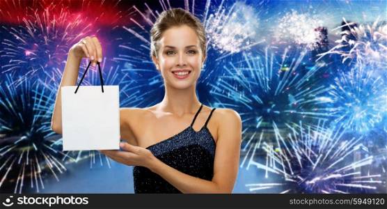 shopping, luxury, advertisement, holydays and sale concept - smiling woman with white blank shopping bag over nigh city and firework background