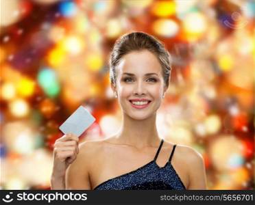 shopping, luxury, winter holidays, christmas and people concept - smiling woman in evening dress holding credit card over red lights background
