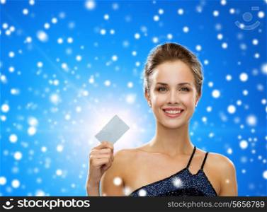 shopping, luxury, winter holidays, christmas and people concept - smiling woman in evening dress holding credit card over blue snowy background