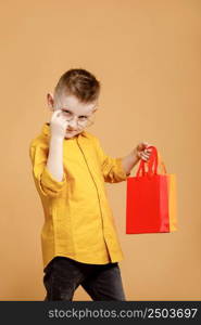 Shopping on black friday. Little boy holding shopping bags on yellow background. Shopper with many colored paper bags. Holidays sales and discounts. Cyber monday. High quality photo.. Shopping on black friday. Little boy holding shopping bags on yellow background. Shopper with many colored paper bags. Holidays sales and discounts. Cyber monday. High quality photo