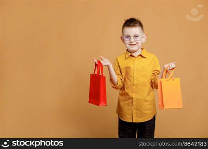Shopping on black friday. Little boy holding shopping bags on yellow background. Shopper with many colored paper bags. Holidays sales and discounts. Cyber monday. High quality photo.. Shopping on black friday. Little boy holding shopping bags on yellow background. Shopper with many colored paper bags. Holidays sales and discounts. Cyber monday. High quality photo