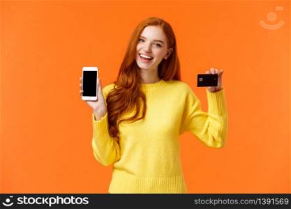 Shopping, online and finance concept. Cheerful young redhead female opened bank account, holding smartphone and credit card, smiling, recommend use online shopping application.. Shopping, online and finance concept. Cheerful young redhead female opened bank account, holding smartphone and credit card, smiling, recommend use online shopping application